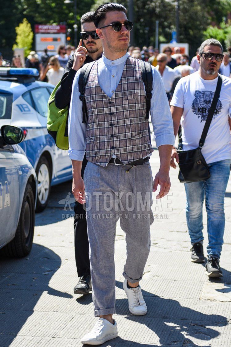 Men's spring/summer coordinate and outfit with plain black sunglasses, gray checked gilet, plain light blue shirt with band collar, plain black leather belt, plain gray slacks, and white low-cut sneakers.