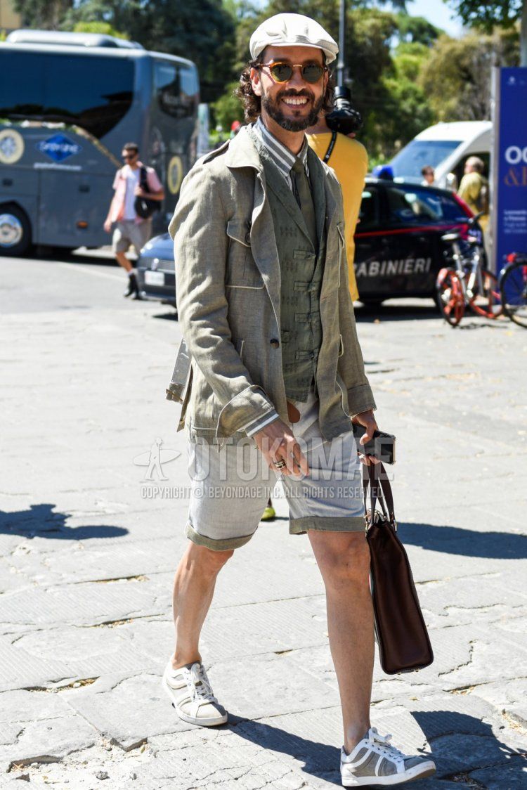 Solid white cap, solid brown sunglasses, linen olive green solid safari jacket, olive green top/inner gilet, olive green/white striped shirt, solid gray shorts, white/gray low cut sneakers, solid brown brief case/handbag, olive green solid color tie, spring/summer men's coordinate and outfit.