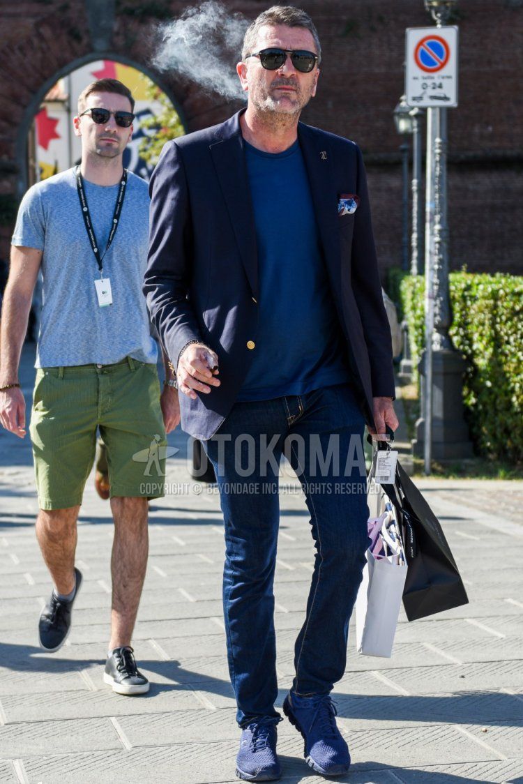Men's spring/summer/autumn coordinate and outfit with plain black sunglasses, plain navy tailored jacket, plain blue t-shirt, plain navy denim/jeans, and navy low-cut sneakers.