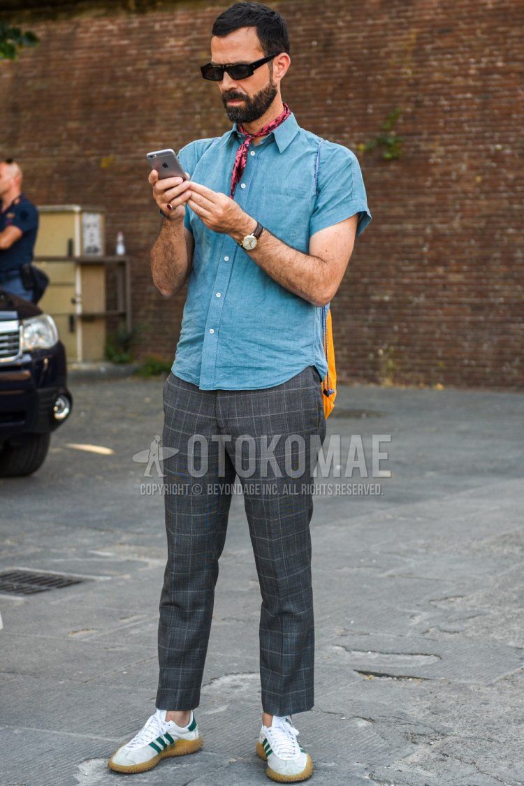 Summer men's coordinate and outfit with square solid black sunglasses, solid red bandana/neckerchief, solid blue denim/chambray shirt, solid gray slacks, and white low-cut Adidas sneakers.