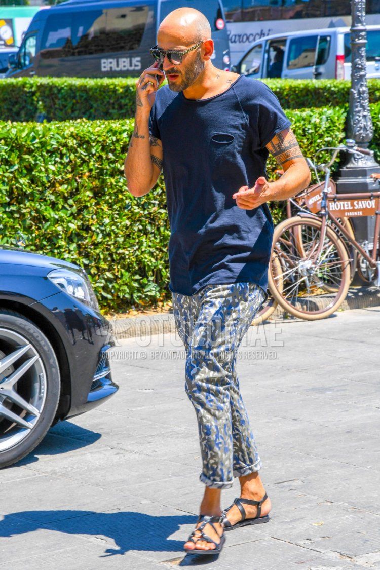 Men's summer coordinate and outfit with plain navy t-shirt, blue/gray bottom cotton pants, and black leather sandals.