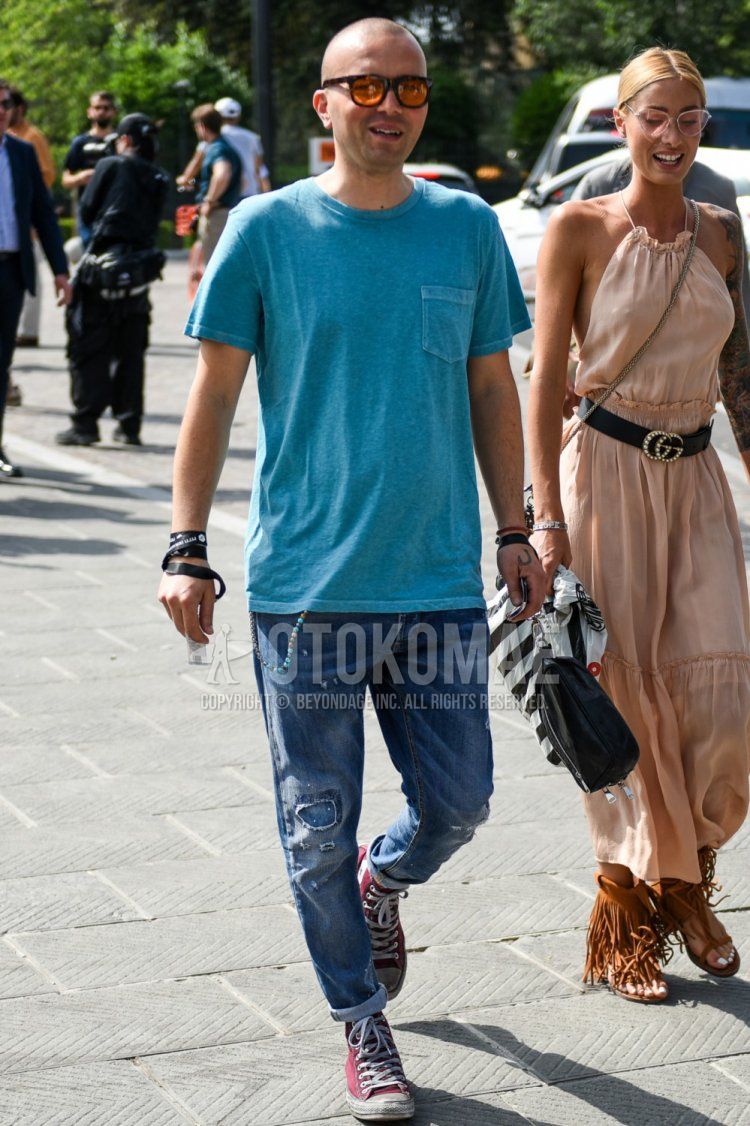 A summer men's coordinate and outfit with plain sunglasses, plain light blue t-shirt, plain blue damaged jeans, and Converse All Star red high-cut sneakers.