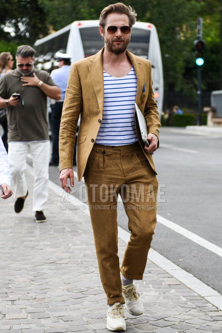 Teardrop brown solid sunglasses, linen brown solid tailored jacket, white/blue border t-shirt, linen brown solid ankle pants, linen brown solid beltless pants, linen brown solid slacks, gray striped socks, Beige low-cut sneakers with beige low-cut sneakers for men's spring and summer outfits.