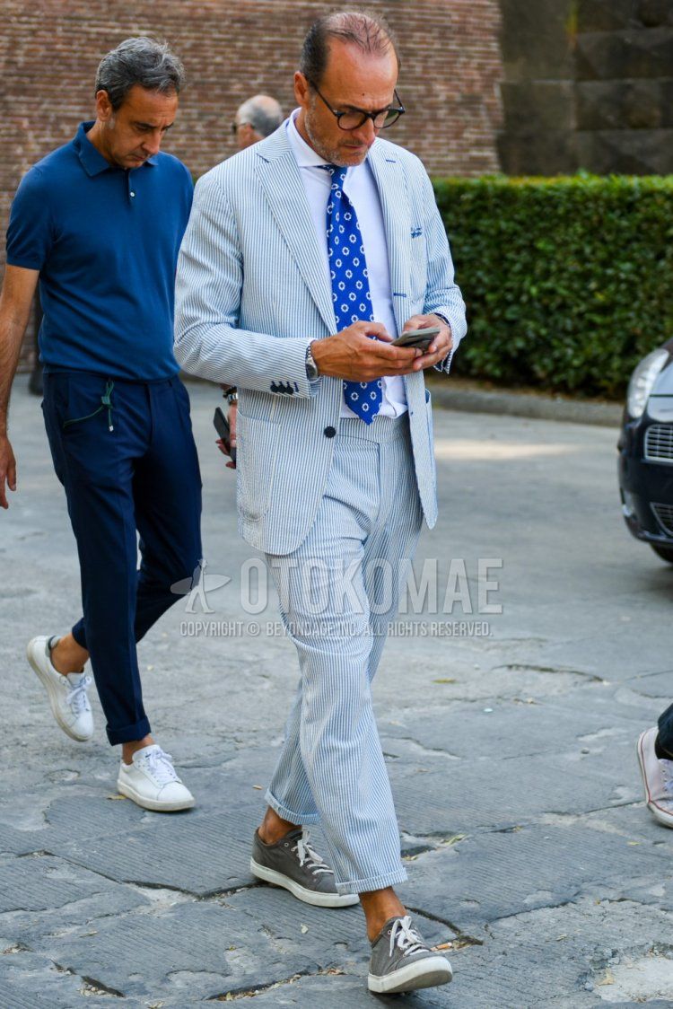 Men's spring/summer/fall coordination and outfit with plain black glasses, plain white shirt, gray low-cut sneakers, light blue striped suit, and blue dot tie.