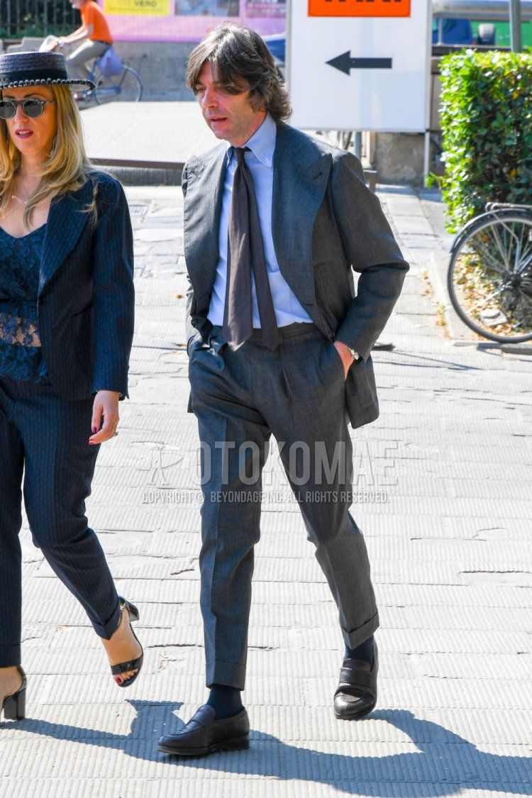 Men's spring and autumn coordination and outfit with plain blue shirt, plain black socks, brown coin loafer leather shoes, plain gray suit, and plain gray tie.