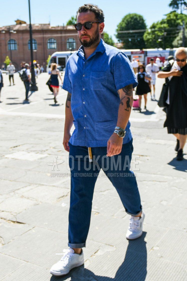 A summer men's coordinate and outfit with plain black sunglasses from Boston, plain blue linen shirt, plain blue denim/jeans, and white low-cut sneakers.