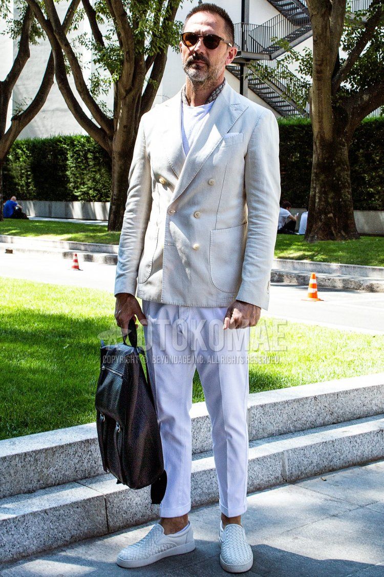 Men's spring/summer/fall outfit with brown tortoiseshell sunglasses, brown graphic bandana/neckerchief, plain white tailored jacket, plain white t-shirt, plain white cotton pants, white slip-on sneakers, and plain brown backpack.