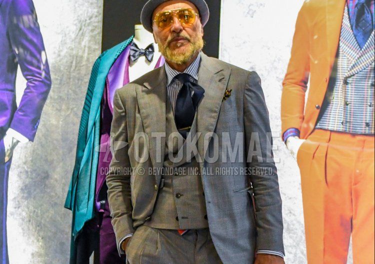 Men's winter coordinate and outfit with plain gray hat, plain glasses, white striped shirt, black brogue shoes leather shoes, plain gray three-piece suit, and plain navy tie.