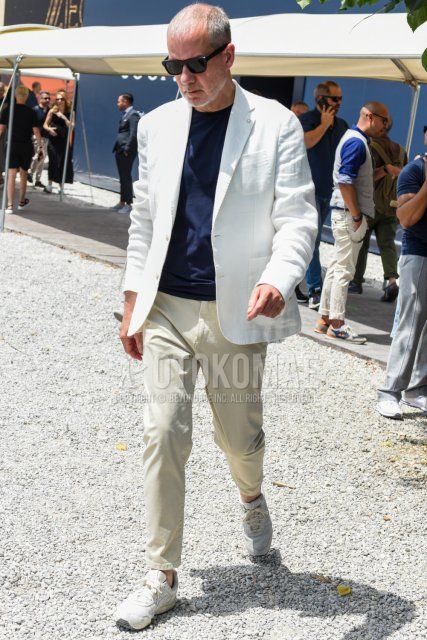 Men's spring, summer, and fall coordinate and outfit with plain black sunglasses, plain white tailored jacket, plain navy t-shirt, plain beige cotton pants, and white low-cut sneakers.