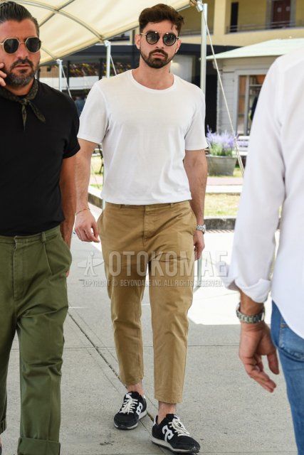 Men's summer coordinate and outfit with plain black/gold sunglasses, plain white t-shirt, plain beige chinos, and black low-cut sneakers.