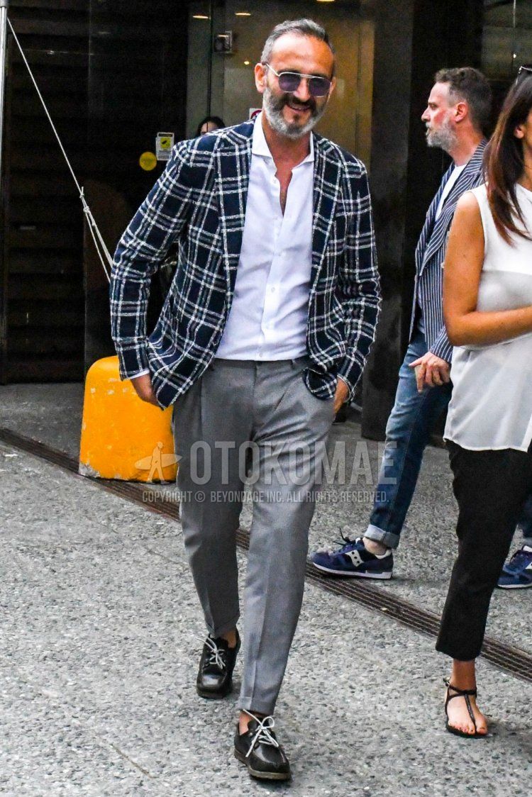 Men's spring/summer/autumn coordination and outfit with plain silver sunglasses, navy check tailored jacket, plain white shirt, plain gray slacks, and black moccasins/deck shoes leather shoes.