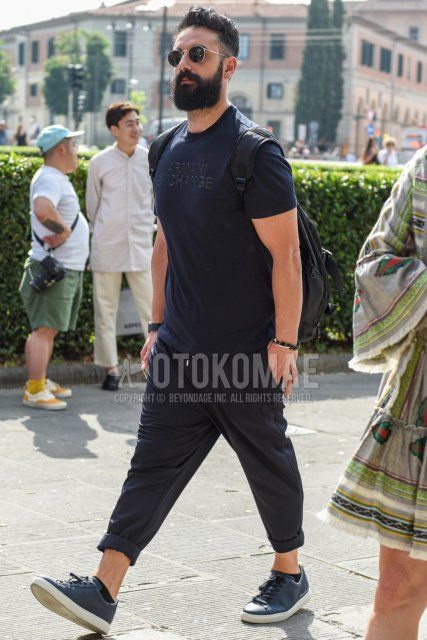 A summer men's coordinate and outfit with round black and gold solid color sunglasses, dark gray graphic t-shirt, dark gray solid color easy pants, and black low-cut sneakers.