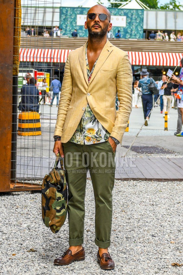 Men's spring/summer/fall outfit with plain sunglasses, plain yellow tailored jacket, white botanical shirt, plain olive green chinos, brown tassel loafer leather shoes, olive green camouflage briefcase/handbag.