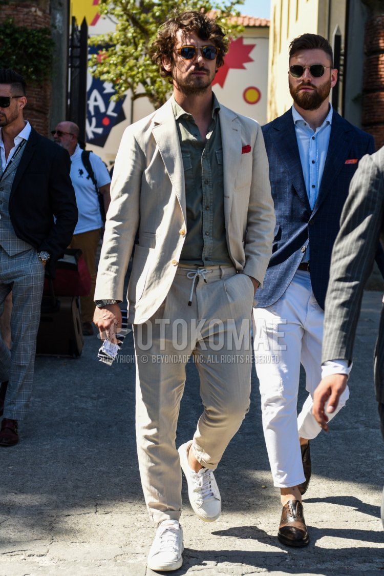 Men's spring, summer, and fall coordination and outfit with plain brown sunglasses, plain olive green shirt, white low-cut sneakers, and plain beige suit.
