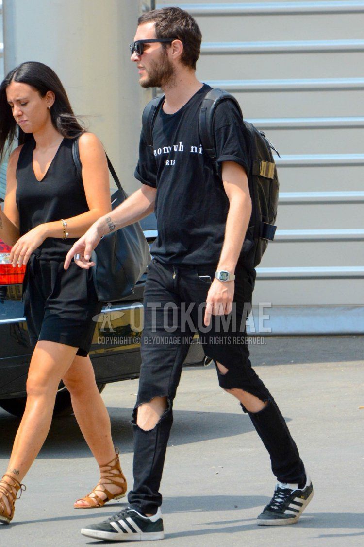 Men's spring/summer coordinate and outfit with plain black sunglasses, black graphic t-shirt, plain black damaged jeans, black low-cut Adidas sneakers, and plain black backpack.