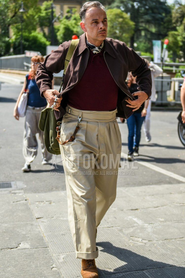 Spring and fall men's coordinate and outfit with beige graphic bandana/neckerchief, solid brown coach jacket, solid red polo shirt, solid beige beltless pants, solid beige chinos, brown suede shoe boots, solid green shoulder bag .