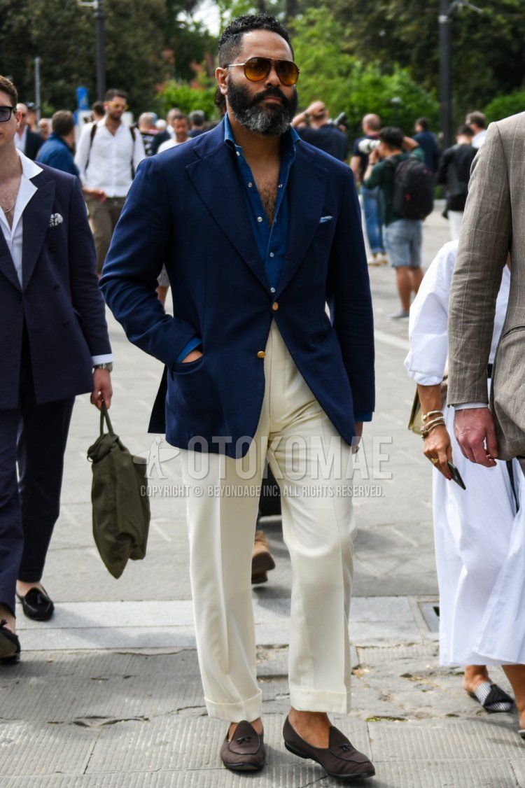 Men's spring/summer/autumn coordinate and outfit with teardrop brown/gold solid sunglasses, solid navy tailored jacket, solid blue denim/chambray shirt, solid white slacks, and brown loafer leather shoes.