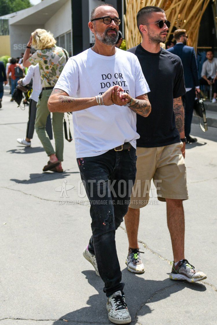 Summer men's coordinate and outfit with plain black glasses, white graphic t-shirt, plain brown mesh belt, plain black/dark gray damaged jeans, and white low-cut Reebok sneakers.