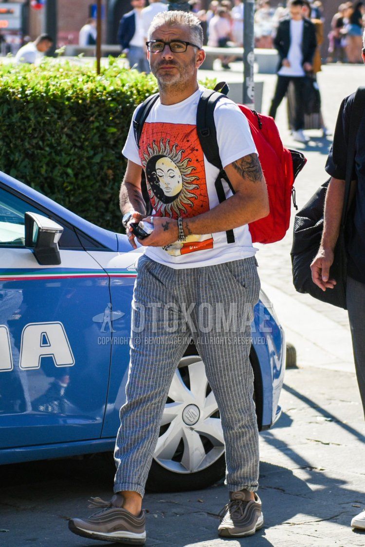 Men's summer coordinate and outfit with plain black glasses, white graphic t-shirt, gray striped slacks, Nike Air Max 95 gray low-cut sneakers, and red plain backpack.