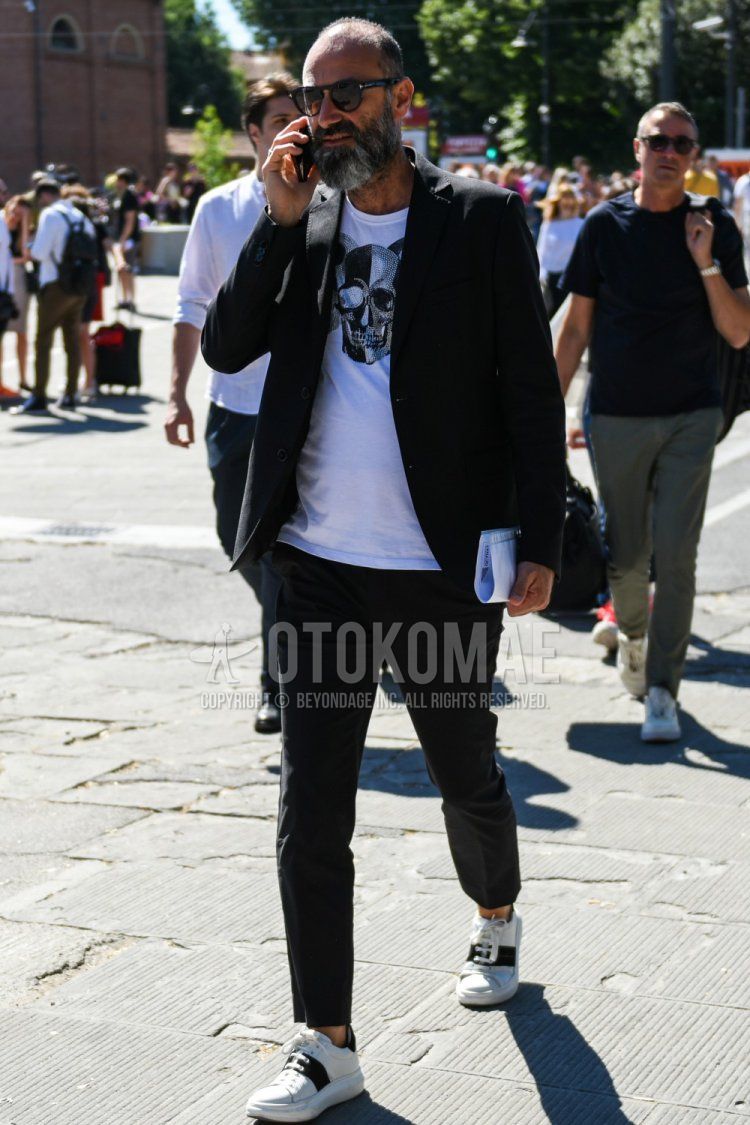 Men's spring, summer, and fall coordination and outfit with Tom Ford plain black sunglasses, white graphic t-shirt, white/black low-cut sneakers, and plain black suit.