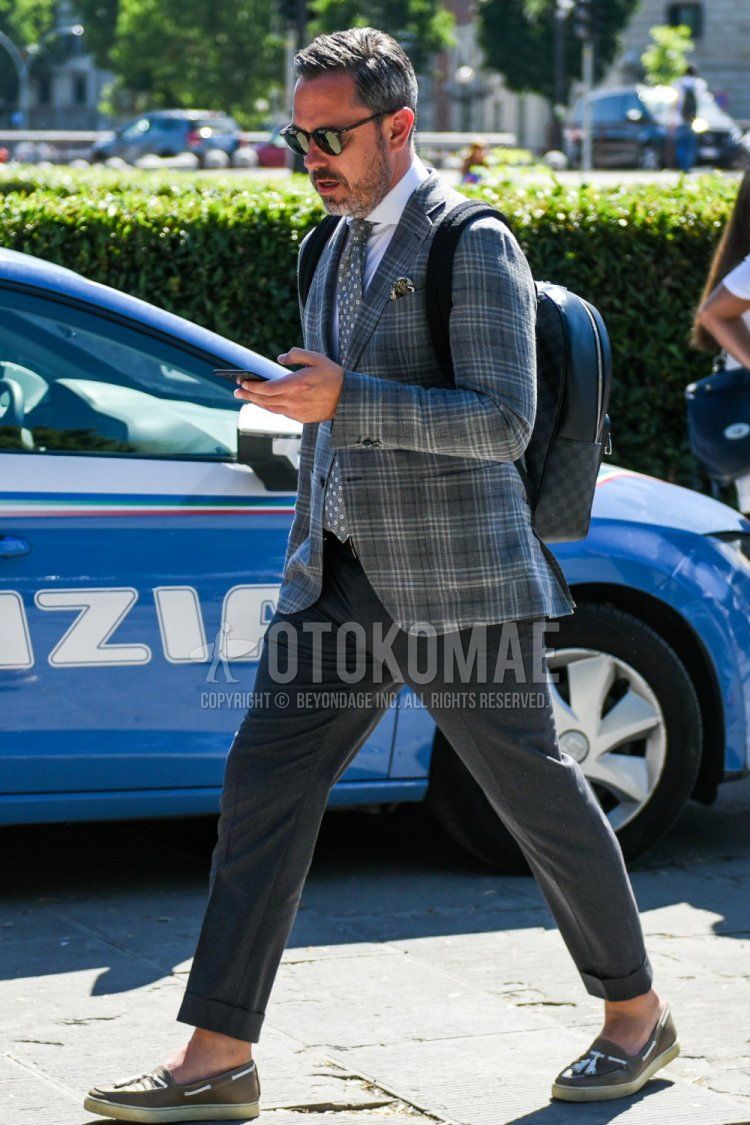 Men's spring and fall outfit with plain black sunglasses from Boston, grey checked tailored jacket, plain white shirt, plain grey slacks, beige slip-on sneakers, Louis Vuitton Damier dark grey and black bag backpack, grey small print tie.