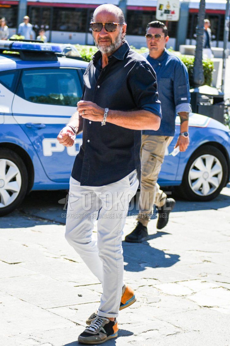 Men's spring/summer coordinate and outfit with brown tortoiseshell sunglasses, plain black shirt, plain beige chinos, and gray/orange low-cut sneakers.