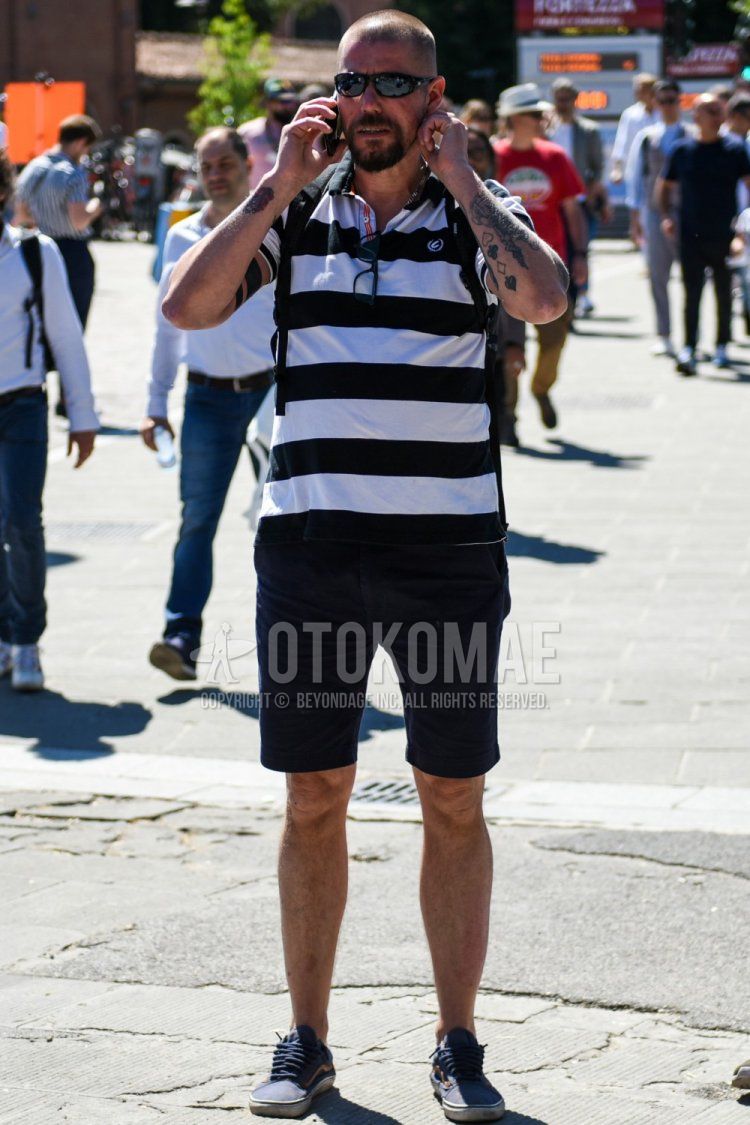Men's summer coordinate and outfit with plain black sunglasses, white/black striped polo shirt, plain navy shorts, plain chinos, and navy low-cut sneakers.