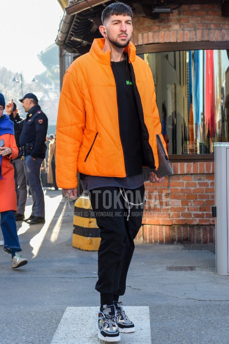 Men's fall/winter outfit with plain orange down jacket, black one-piece sweatshirt, plain gray t-shirt, plain black jogger pants/ribbed pants, plain black easy pants, and gray low-cut sneakers.