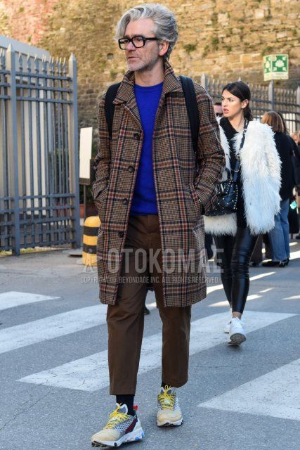 Men's fall/winter outfit with Tom Ford plain black glasses, brown checked stainless coat, plain blue sweater, plain brown slacks, plain brown cropped pants, plain black socks, and multi-colored low-cut sneakers.