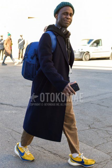 Men's fall/winter outfit with solid green knit cap, solid black chester coat, solid black hoodie, solid beige winter pants (corduroy,velour), solid beige ankle pants, solid white socks, yellow low cut sneakers, solid blue backpack. Outfit.