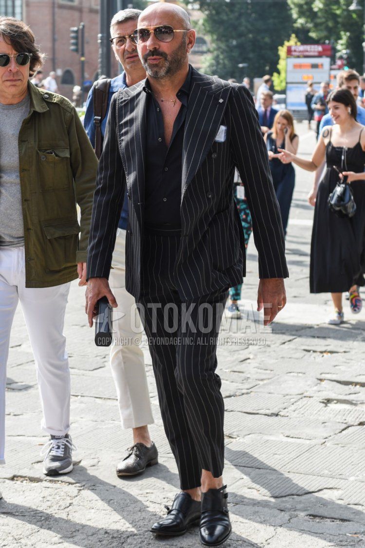 Men's spring, summer, and fall coordination and outfit with plain black and gold sunglasses, plain black shirt, black monk shoes leather shoes, and black striped suit.