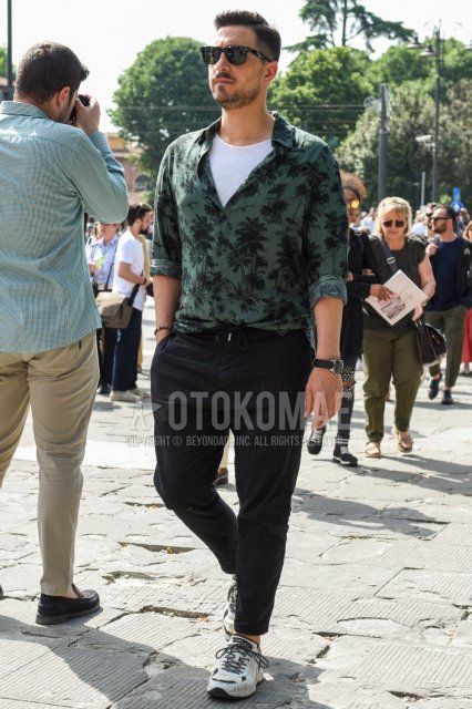 Men's spring, summer, and fall coordinate and outfit with plain black sunglasses, green botanical shirt, plain white t-shirt, plain black easy pants, and white low-cut sneakers.