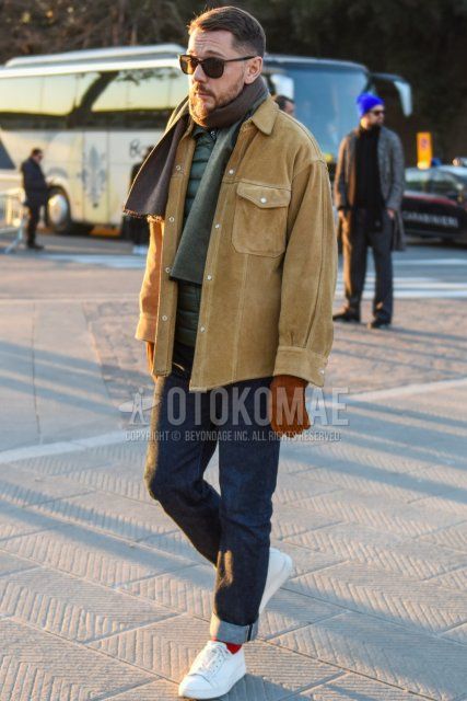 Men's fall/winter outfit with brown tortoiseshell sunglasses, solid gray scarf/stall, solid beige shirt jacket, solid olive green inner down, solid navy denim/jeans, solid red socks, white low-cut sneakers.