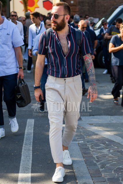 A summer men's coordinate and outfit with plain black sunglasses, navy striped shirt, plain beige cotton pants, and white low-cut sneakers.