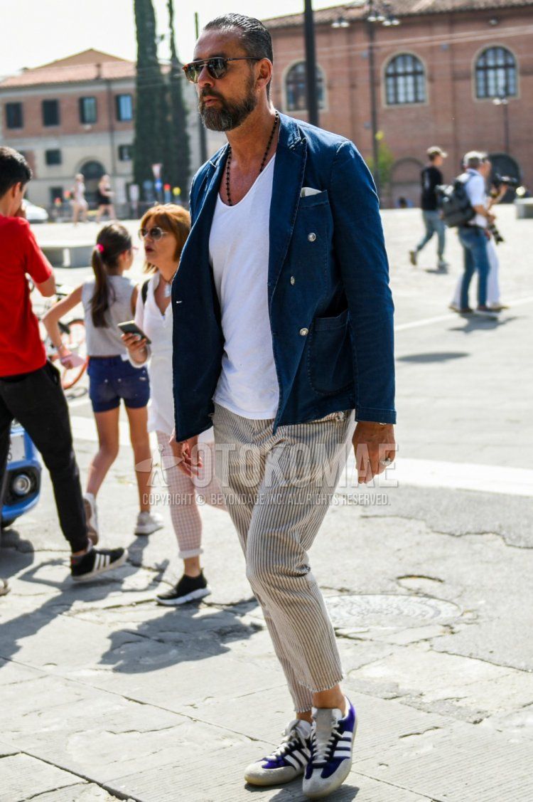 Men's spring and fall coordinate and outfit with brown tortoiseshell sunglasses, plain navy tailored jacket, plain white t-shirt, beige striped cotton pants, and purple low-cut sneakers by Adidas.