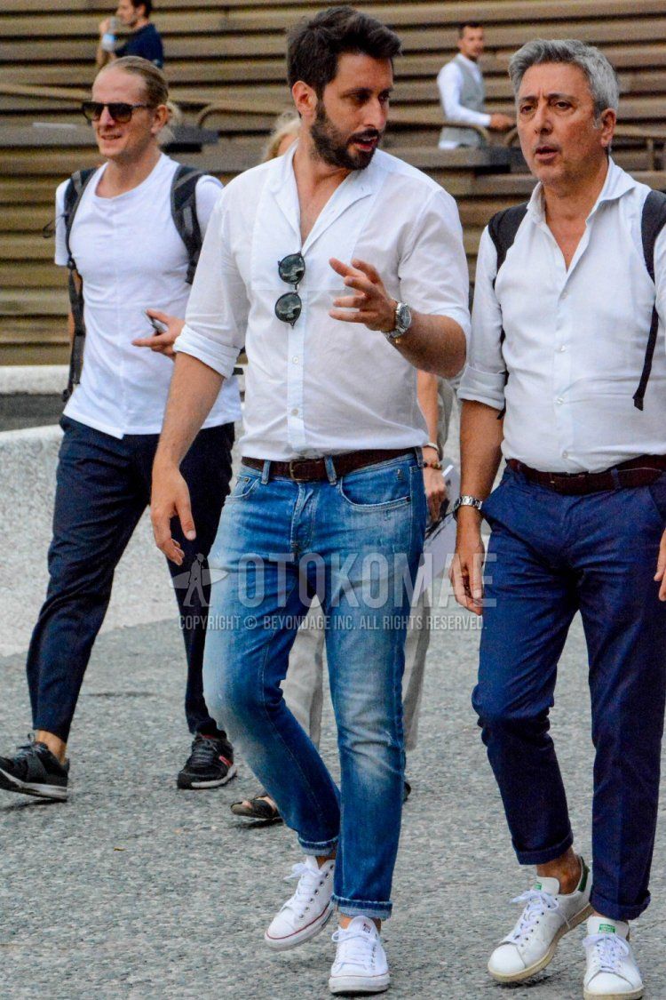 Men's spring/summer coordinate and outfit with plain white shirt, plain brown leather belt, plain blue denim/jeans, and Converse All Star white low-cut sneakers.