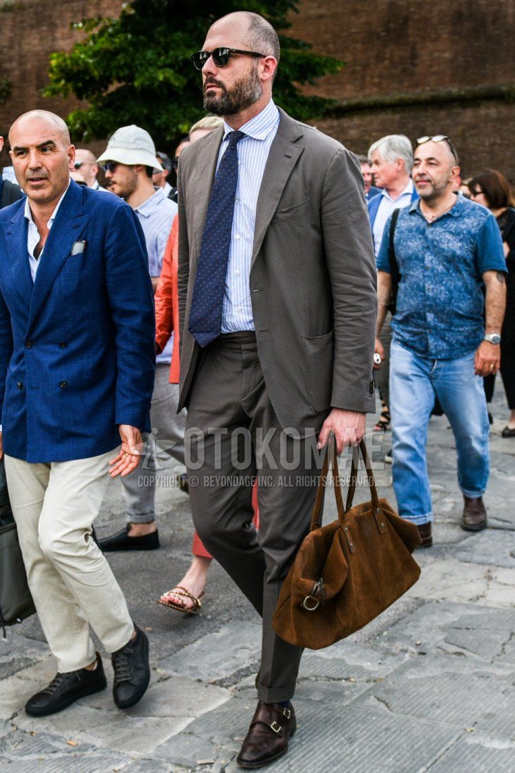 無地のサングラス、白ストライプのシャツ、ブラウンモンクシューズの革靴、ブラウン無地のボストンバッグ、グレー無地のスーツ、ネイビードットのネクタイを合わせた春秋のメンズコーデ・着こなし。