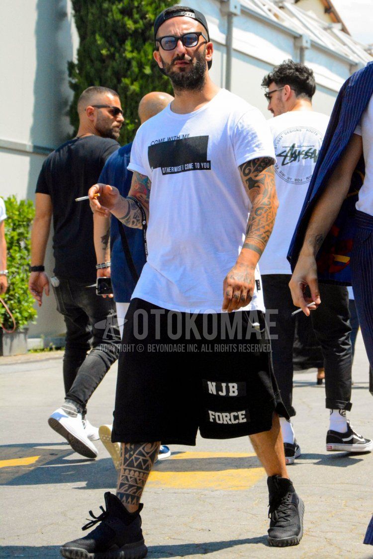 無地のベースボールキャップ、無地のサングラス、白グラフィックのTシャツ、黒グラフィックのショートパンツ、黒ハイカットのスニーカーを合わせた春夏秋のメンズコーデ・着こなし。