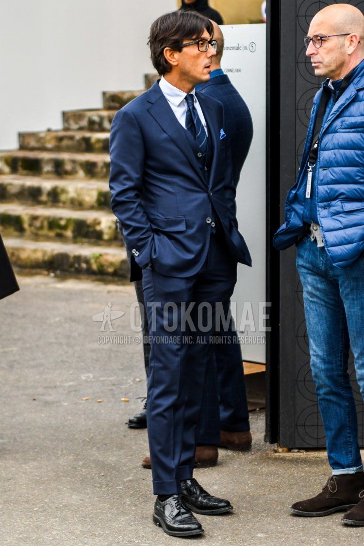 Men's spring and fall coordinate and outfit with plain glasses, plain white shirt, plain black socks, black wingtip leather shoes, plain navy three-piece suit, and navy regimental tie.
