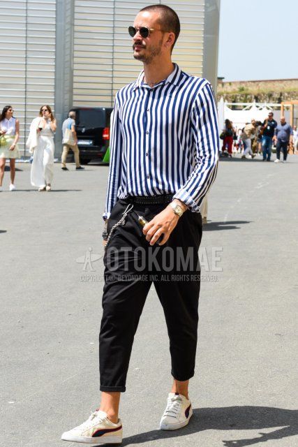 Men's spring/summer coordinate and outfit with plain black sunglasses, white/navy striped shirt, plain black leather belt, dark gray plain slacks, and white low-cut Puma sneakers.