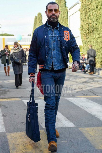 Teardrop gold solid sunglasses, navy lettered stadium jacket, solid blue denim jacket, solid black turtleneck knit, solid navy denim/jeans, suede beige side gore boots, navy graphic tote bag for fall/winter Men's Codes and Outfits.