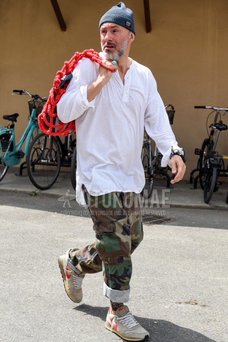 Men's spring, summer, and fall coordinate and outfit with plain gray knit cap, plain white henley-neck long T, multi-colored camouflage cargo pants, and gray/beige low-cut Nike sneakers.