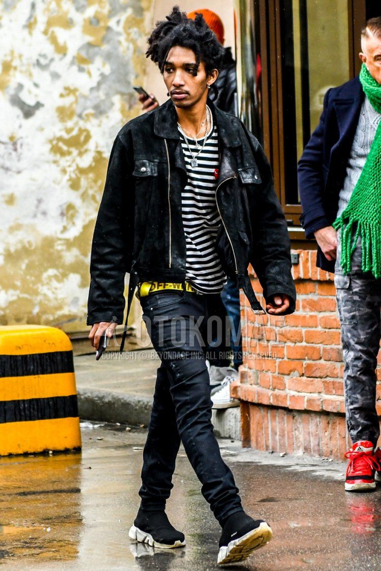 Men's fall/winter outfit with plain black outerwear, Play Comme des Garcons white/black striped long T, off-white yellow graphic tape belt, plain black denim/jeans and Balenciaga Speed Trainers black high-cut sneakers.