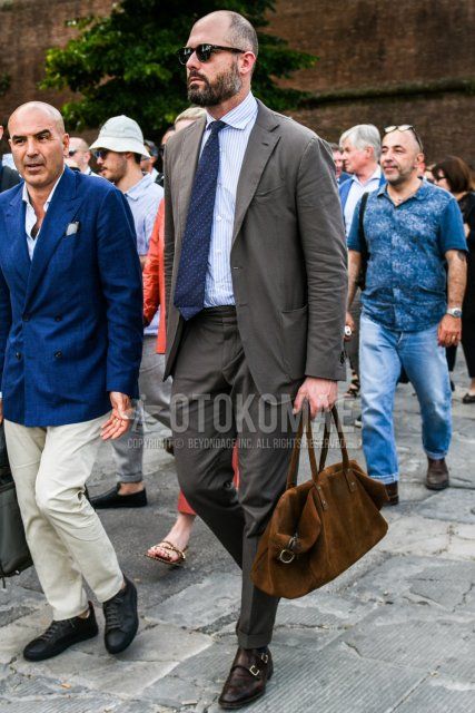 Men's spring and fall coordinate and outfit with plain sunglasses, white striped shirt, brown monk shoes leather shoes, plain brown Boston bag, plain gray suit, and navy dot tie.