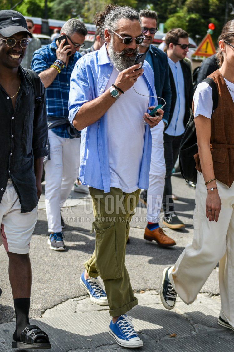 Men's spring/summer coordinate and outfit with clear solid color sunglasses, light blue solid color shirt, white solid color t-shirt, olive green solid color cargo pants, and blue low cut sneakers.
