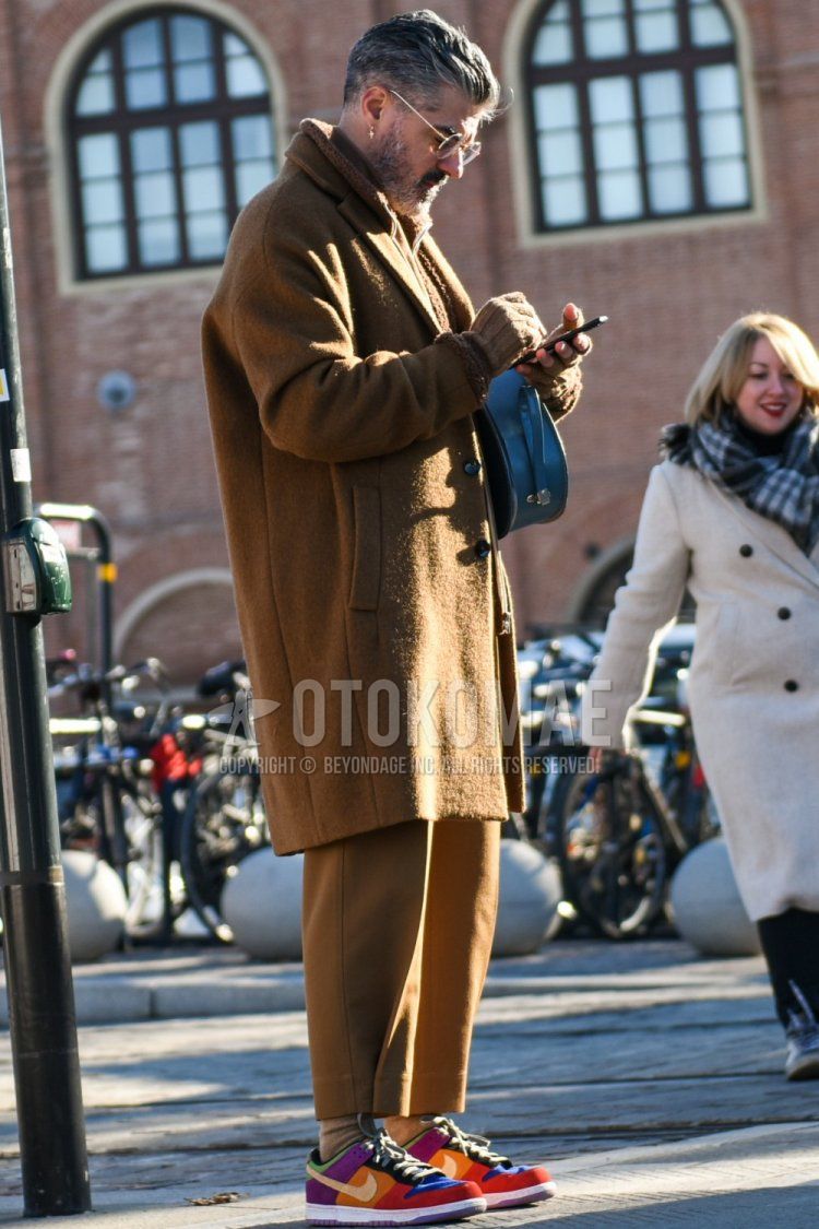 Men's fall/winter coordinate and outfit with plain gold glasses, plain beige chester coat, plain beige cropped pants, plain beige chinos, plain beige socks, and Nike Dunk multi-colored low-cut sneakers.