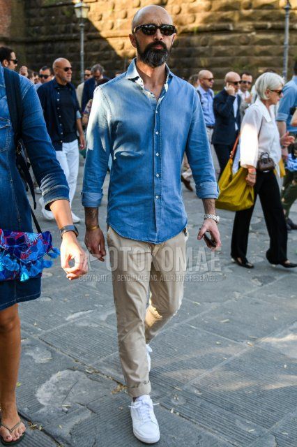 Men's spring/summer coordinate and outfit with solid black sunglasses, solid blue denim/chambray shirt, solid beige cotton pants, and white low-cut sneakers.