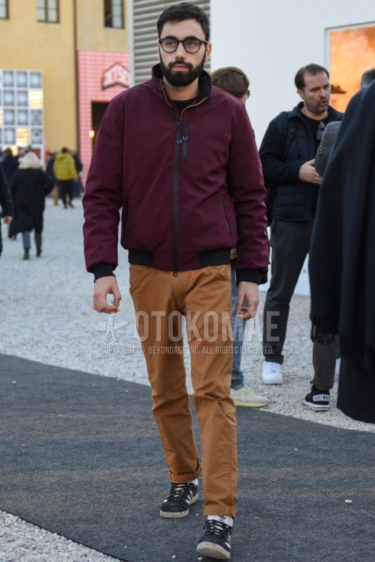 Men's fall/spring coordinate and outfit with plain black glasses, plain red windbreaker, plain beige chinos, and Adidas gray low-cut sneakers.
