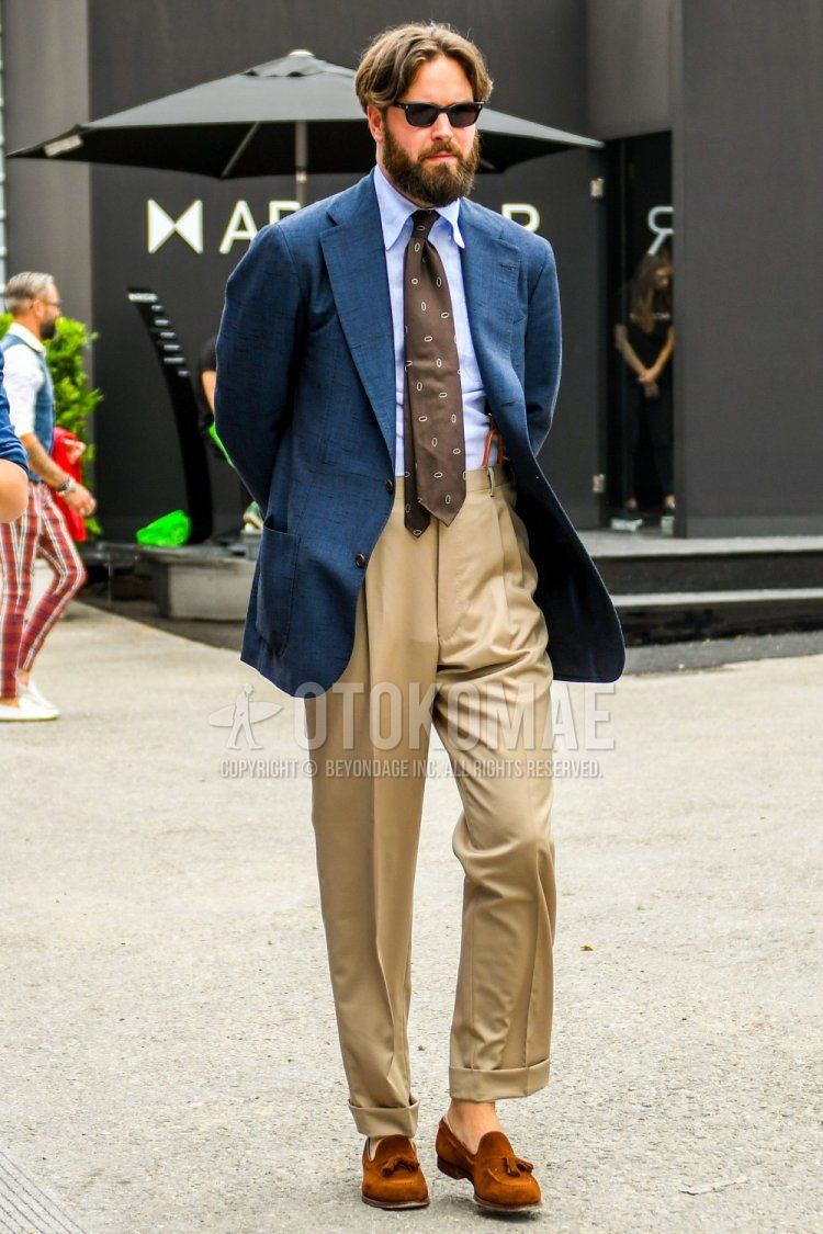 Men's spring/summer/fall outfit with plain black sunglasses, plain navy tailored jacket, plain light blue shirt, suspenders, plain beige beltless pants, pleated pants, beige tassel loafer leather shoes, beige/brown small print tie.