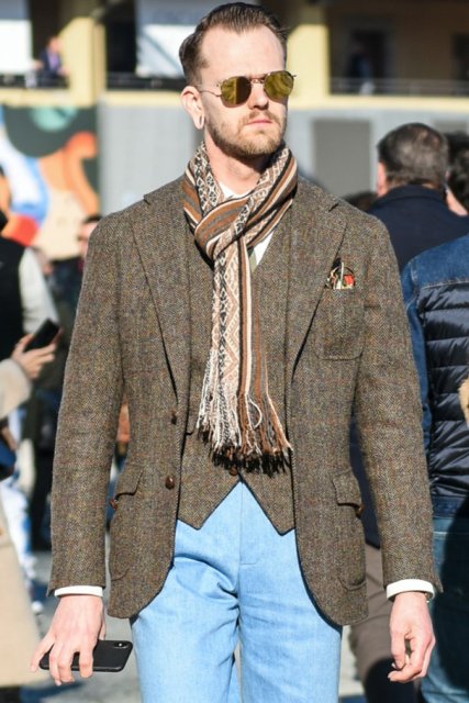 Teardrop plain silver sunglasses, beige-brown scarf/stall, gray-brown herringbone tailored jacket, gray-brown herringbone gilet, solid light blue slacks, solid light blue ankle pants, solid navy socks, suede brown tassel loafer leather shoes for men in fall and winter.